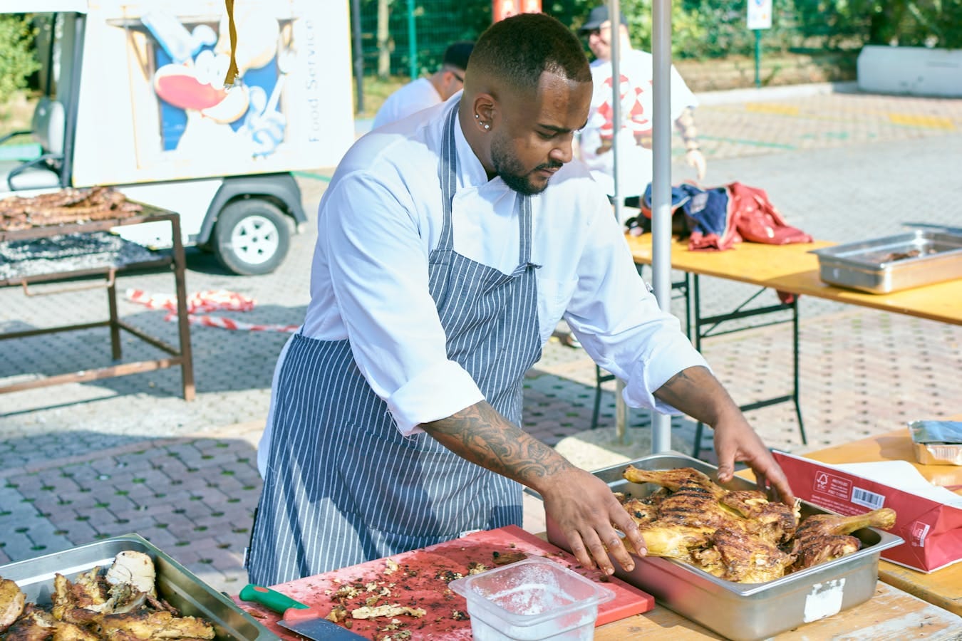 Professional chef arranging grilled chicken at outdoor food event.
