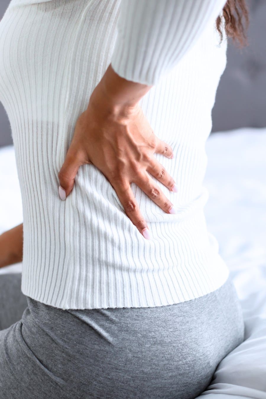 Woman with side back pain sitting on bed at home