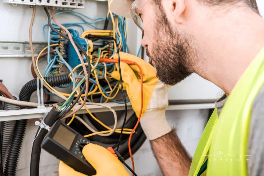 side view of electrician checking electrical box with multimeter in corridor
