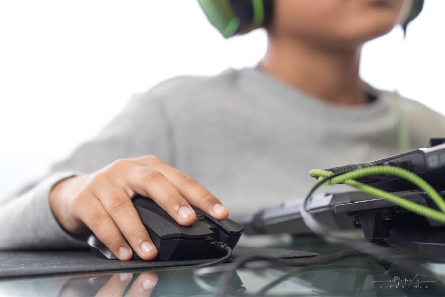 child with hand on mouse and wearing headphones while playing video game on computer