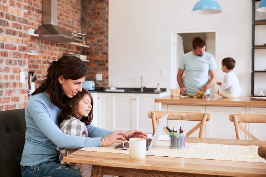 Busy Family Home With Mother Working As Father Prepares Meal