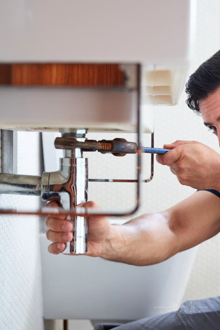 Male Plumber Using Wrench To Fix Leaking Sink In Home Bathroom