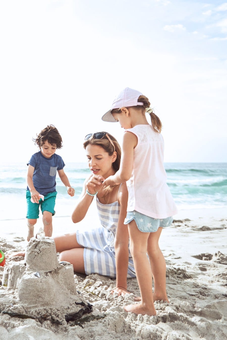 siblings building sandcastle at beach with mom