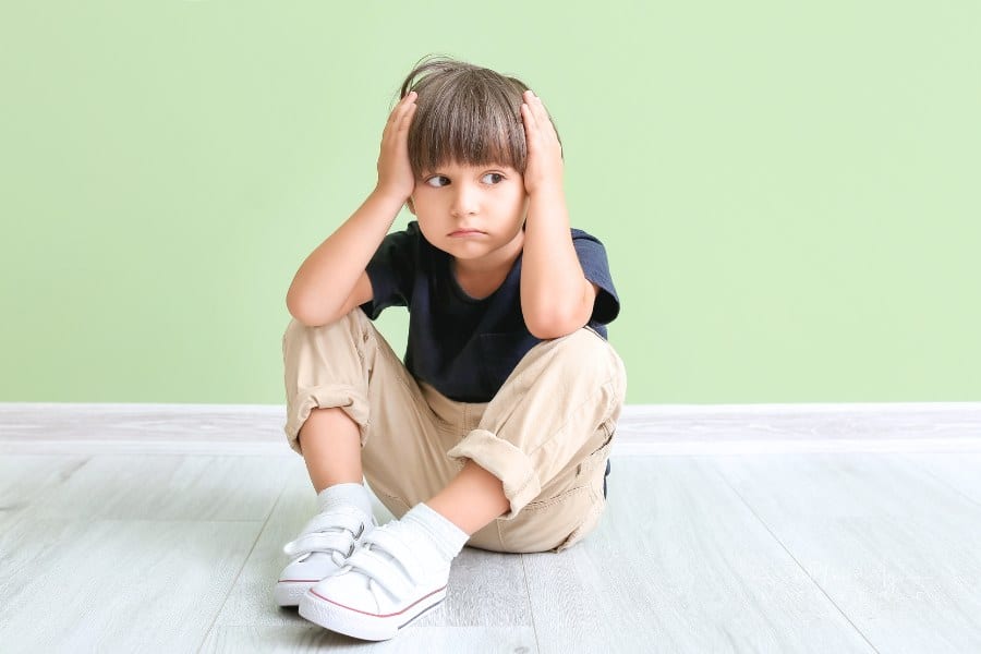 little boy covering his ears in front of a light green wall