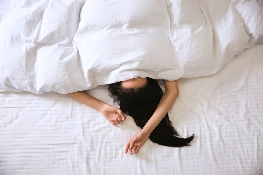 woman laying under blanket with head covered and arms over her head