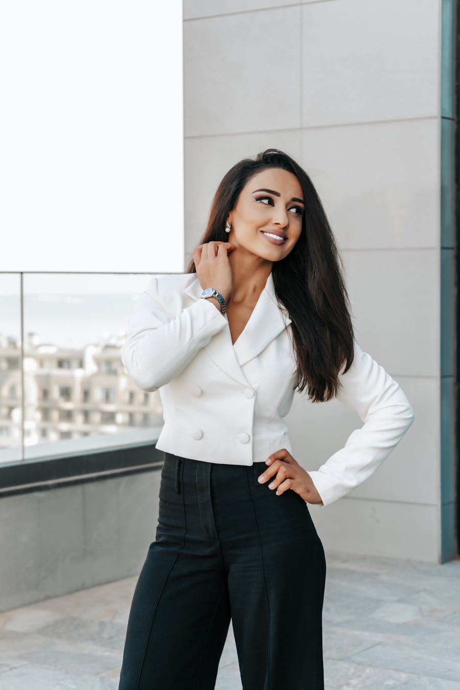 Smiling woman in a chic outfit posing on a modern rooftop terrace.