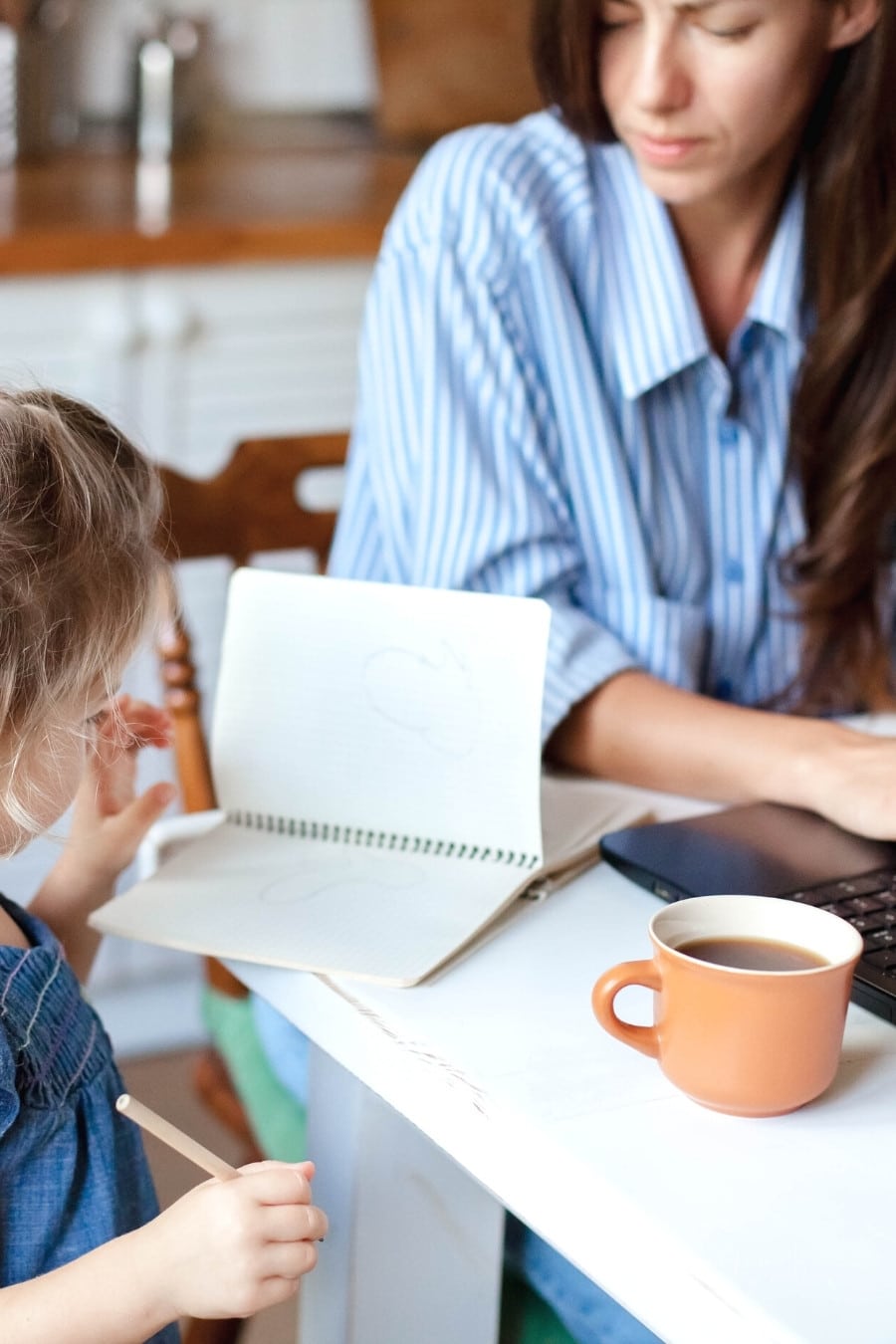 working mom on laptop with child drawing nearby