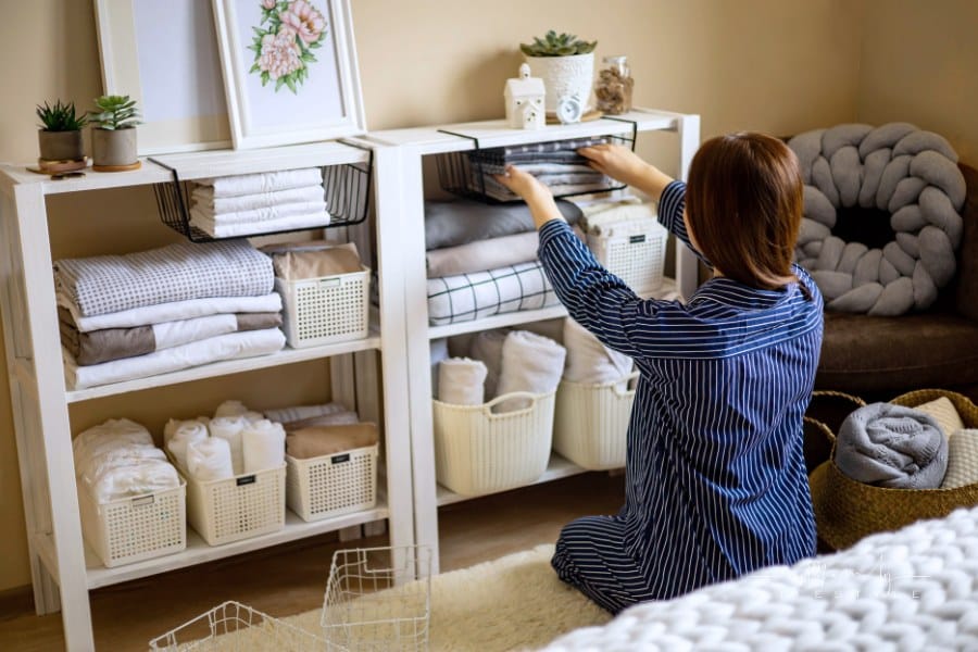 woman in pajamas neatly putting folded linens into cupboard vertical storage Marie Kondo