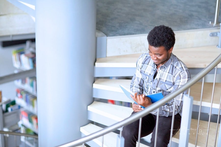 man reading a book on stairs at the library