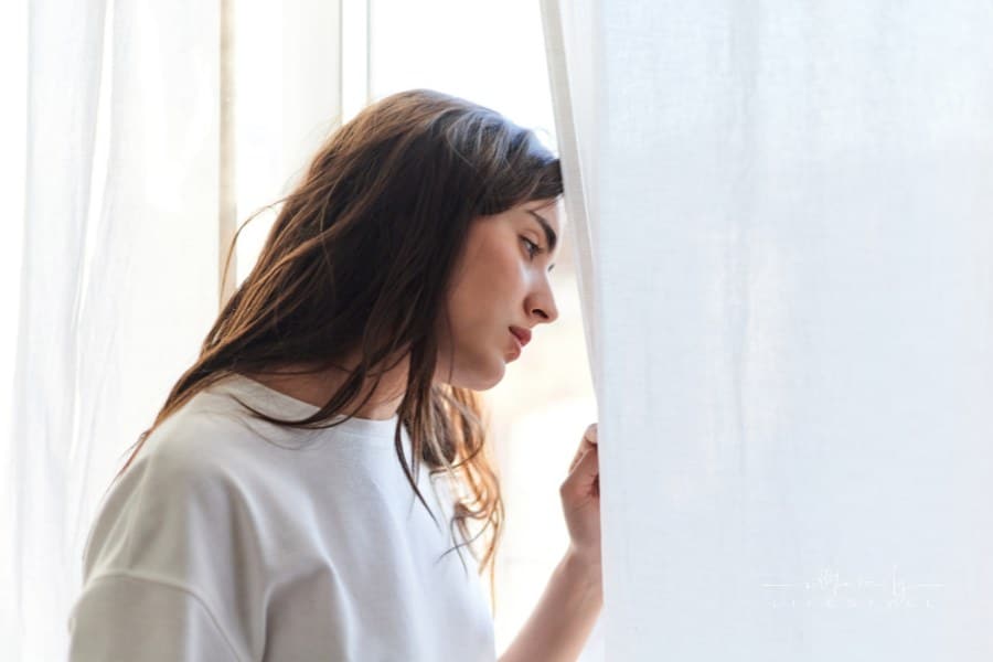 Sad young woman looking out a window at home. Mental health concept.