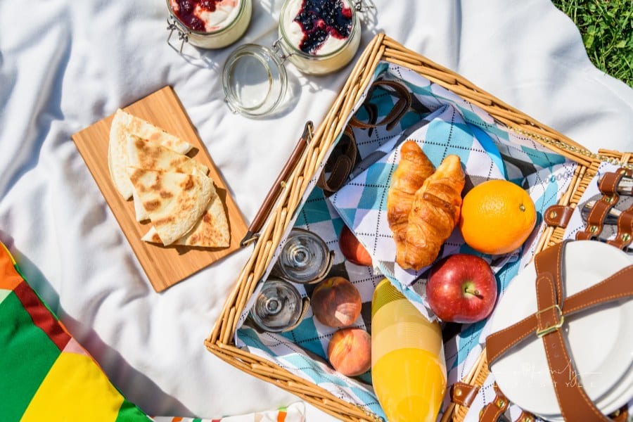 Picnic basket with fruits, orange juice, croissants, quesadilla and no bake blueberry and strawberry jam cheesecake