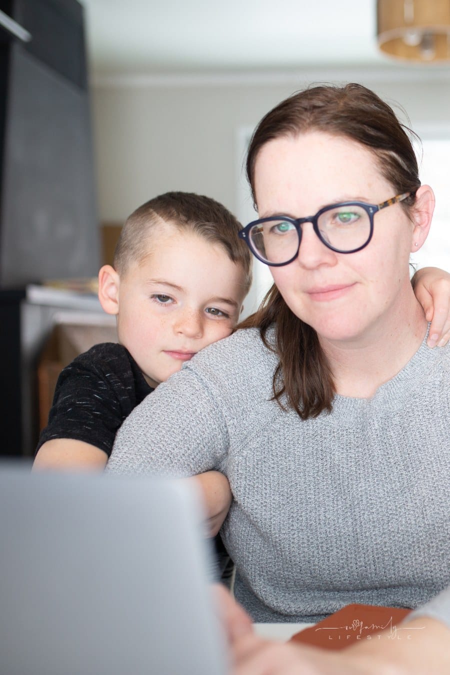 young son hugging mom while she is on the computer