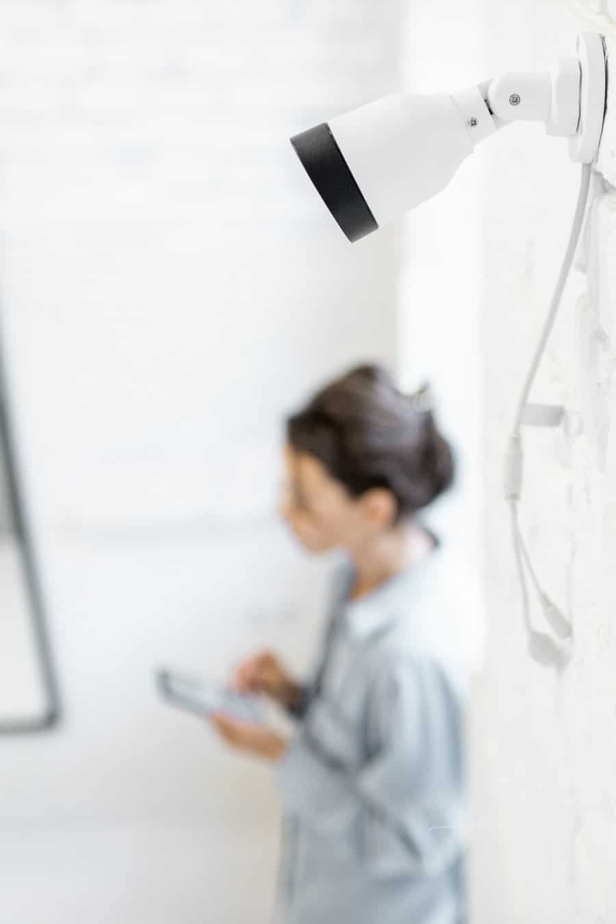 Woman controls home video surveillance with a smartphone indoors, view from the above and ip camera on the foreground. Concept of a wireless home security systems