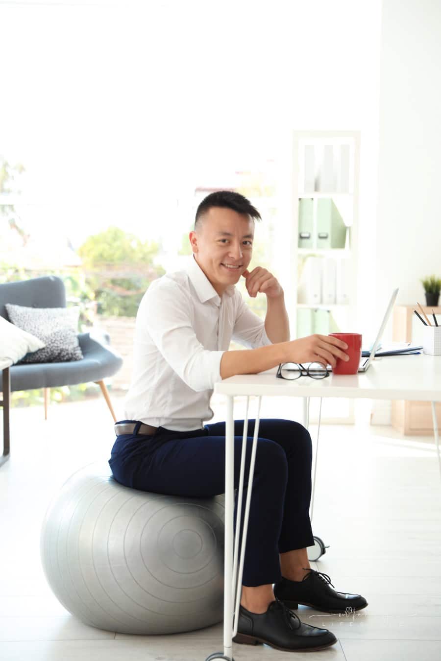 Happy young businessman sitting on fitness ball in office. Workplace exercises