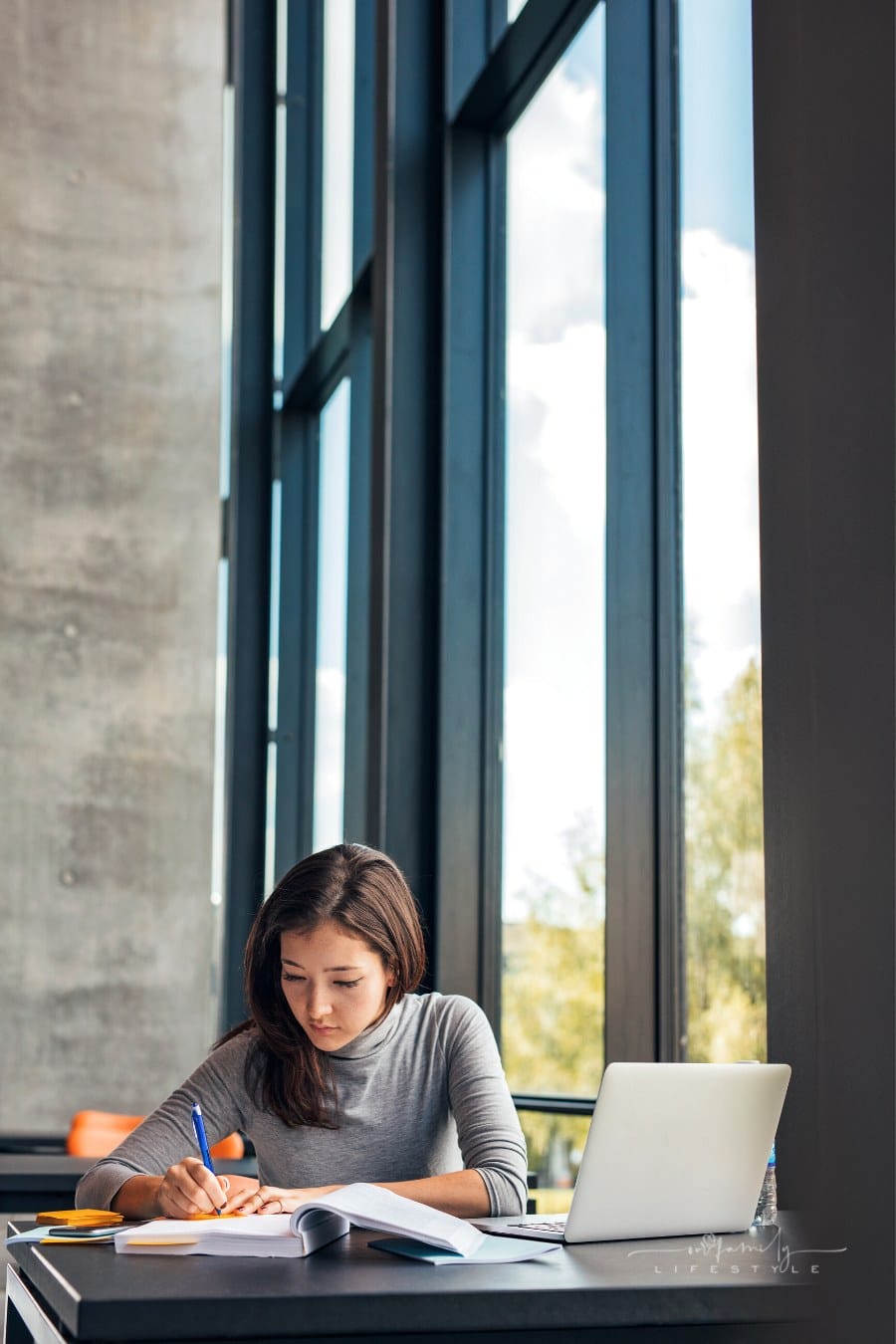 college student taking notes from books in library as she studies