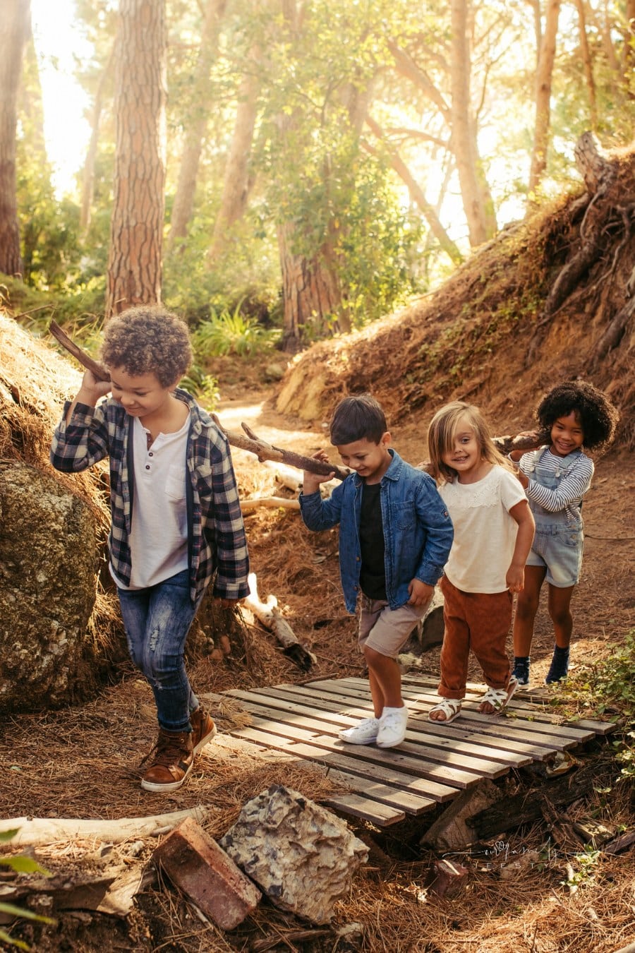 Group of children building camp in forest together. Boys and girls carrying sticks and walking