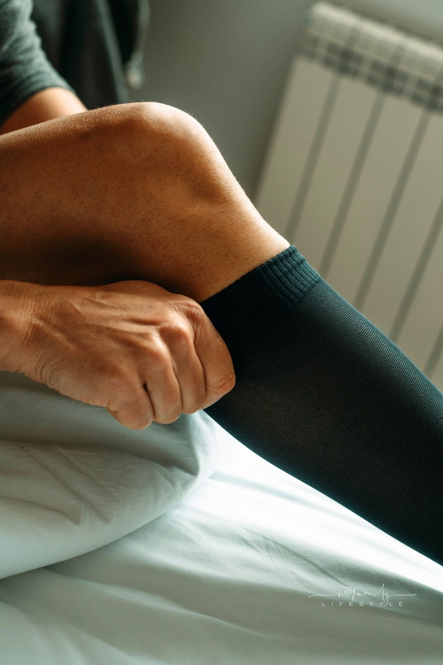 man sitting on the bed putting on a compression sock