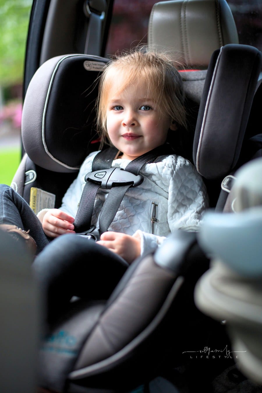 Happy toddler sitting in her booster seat in the backseat of car