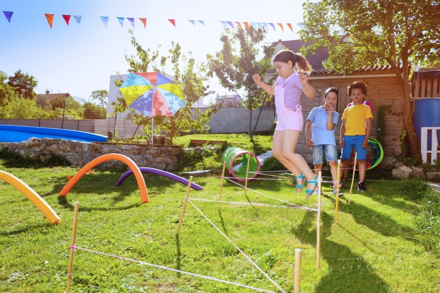 Girl jumps in over strings in sequence of obstacles game on playground in a group of kids