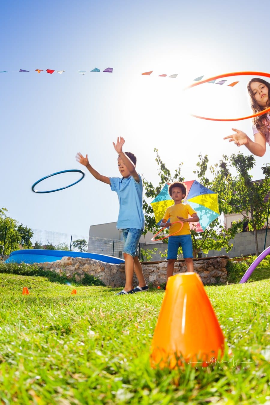 Group of diverse play target practicing game with hula hoops rings on the lawn of playground