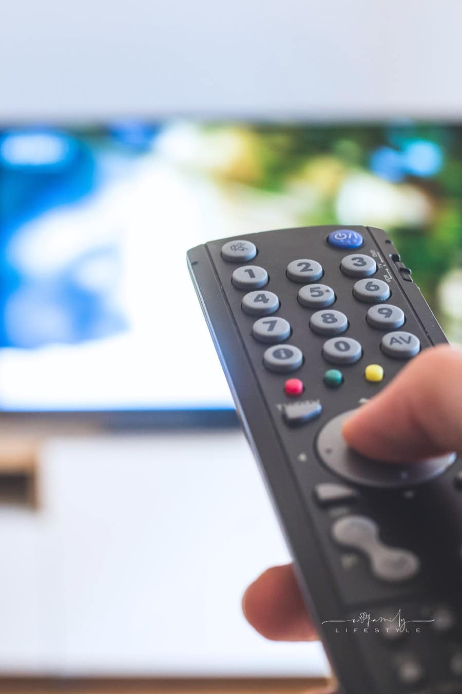 Male hand is holding TV remote control, streaming on a smart TV.