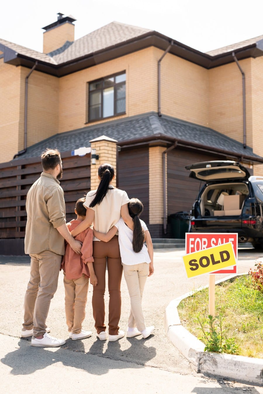 Rear view of young family embracing each other against new house and dreaming of new life