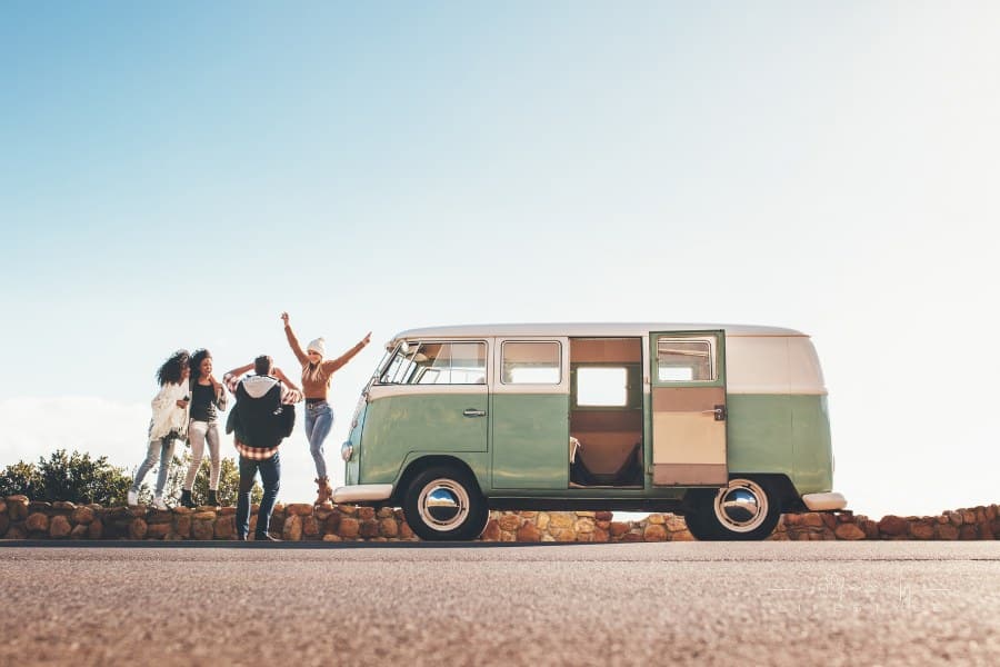 Group of friends on road trip together. Old minivan parked on highway with friends taking pictures outdoors. Man taking photo