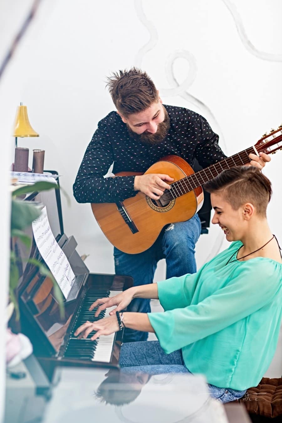 man playing a guitar accompanied by woman on piano while both laugh