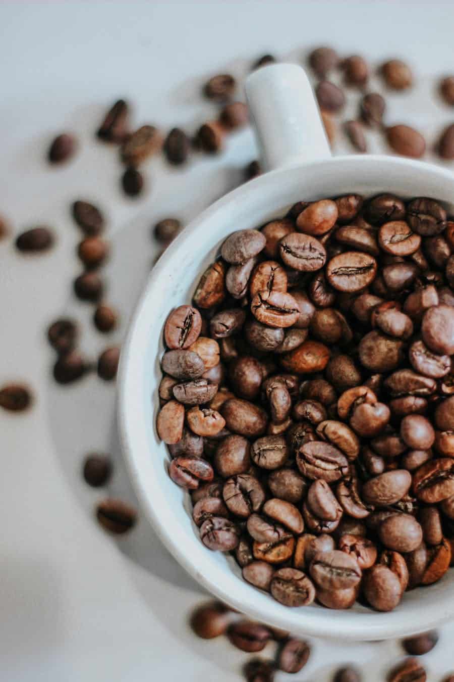 Top view of roasted coffee beans filling and surrounding a white cup.