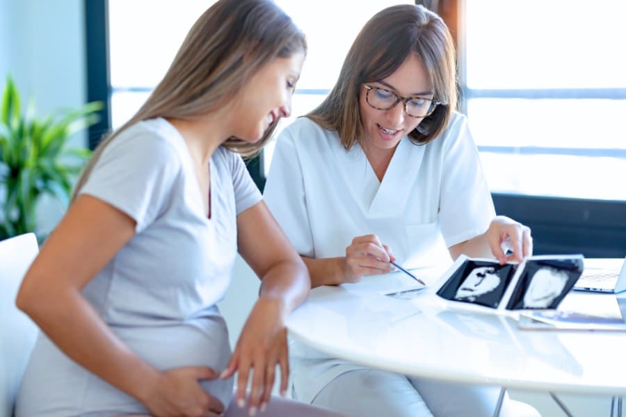 Young Woman Gynecologist Doctor Showing to Pregnant Woman Ultrasound