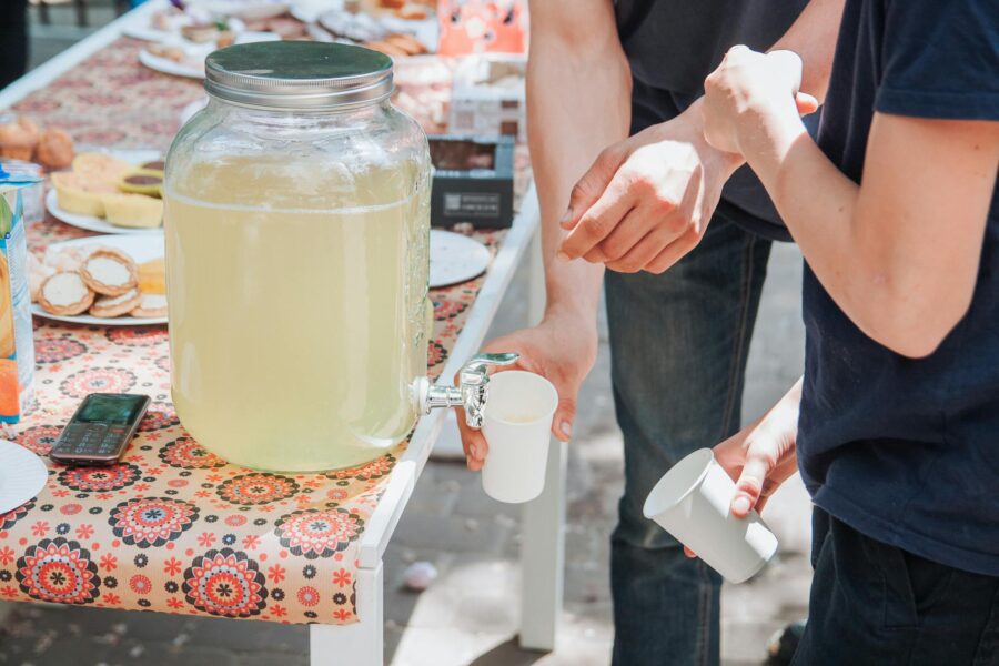 Two people serving lemonade at an outdoor picnic table with snacks, capturing a summer vibe.