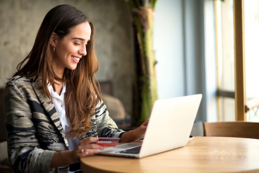 smiling woman using laptop in cafe holding credit card in her hand