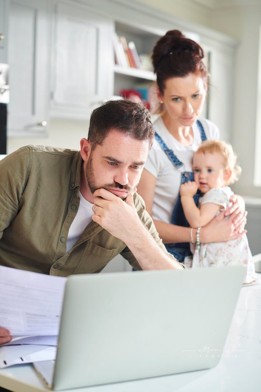 dad unhappy while looking over family finances with mom and baby in background