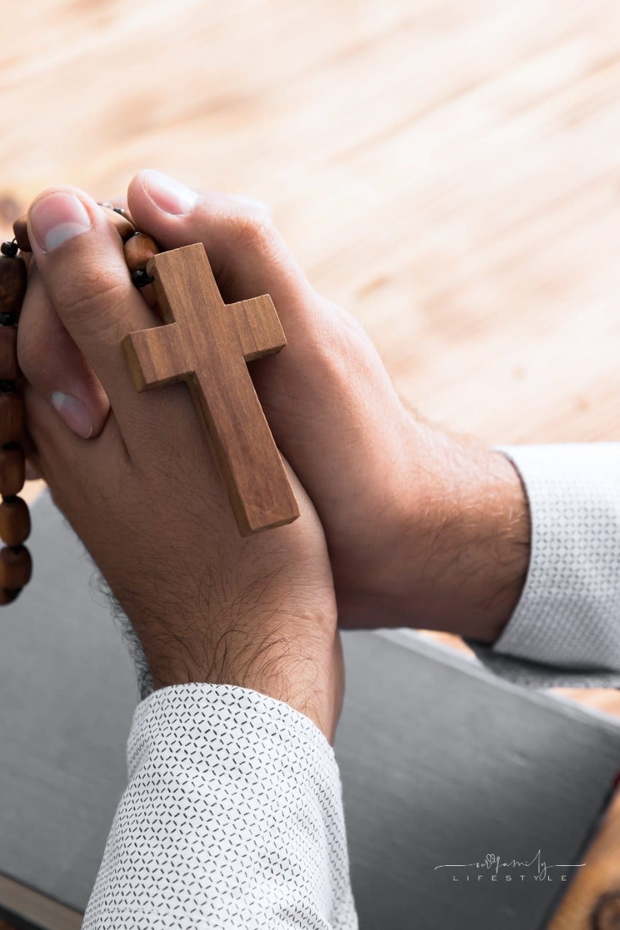 man's praying hands holding a rosary over a Bible