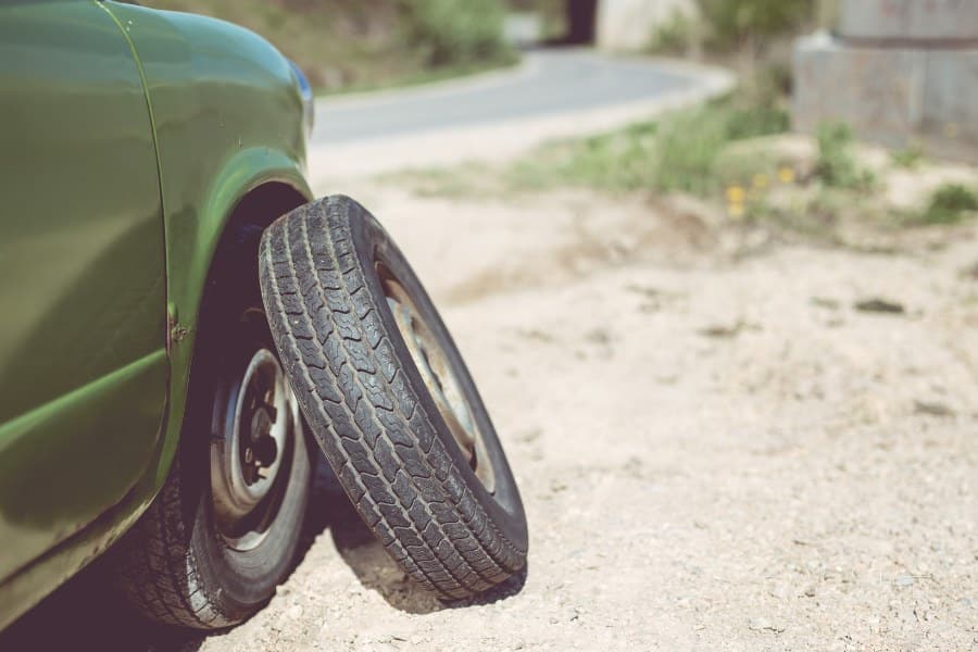 Front end of a green mini car with a spare wheel leaned onto it