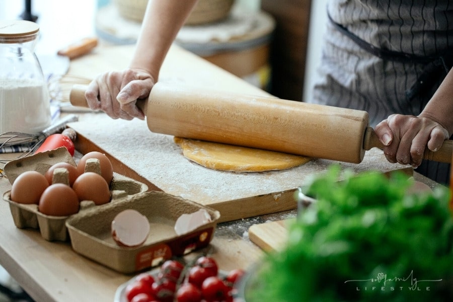 woman using rolling pin on dough in kitchen