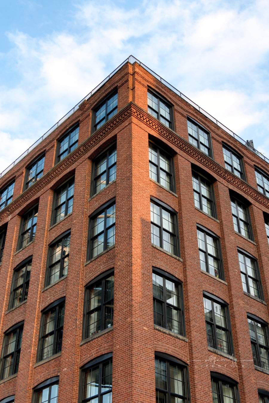 Low angle view of tall brick apartment building with beautiful blue sky and clouds reflecting in windows