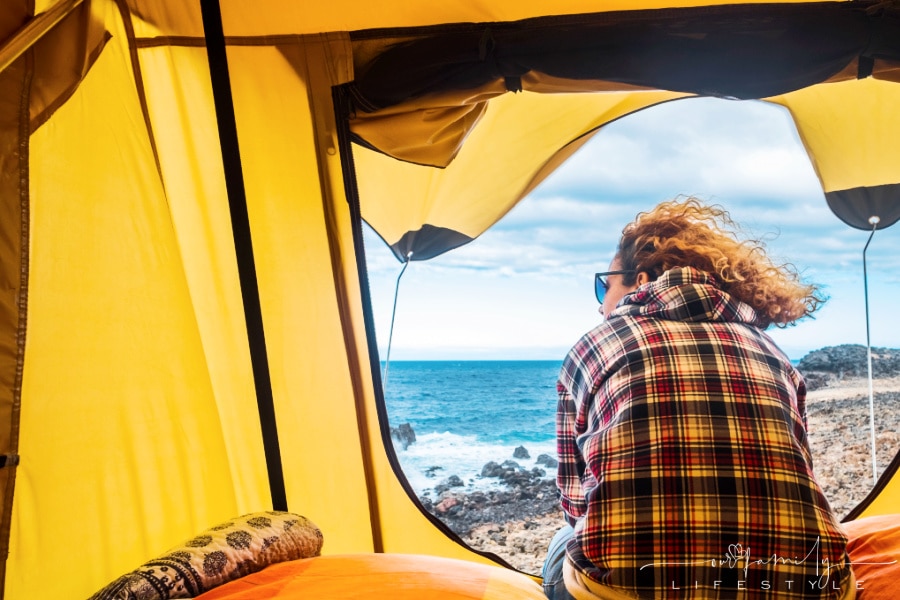 view-of-woman-sitting-outside-tent-on-rocky-beach
