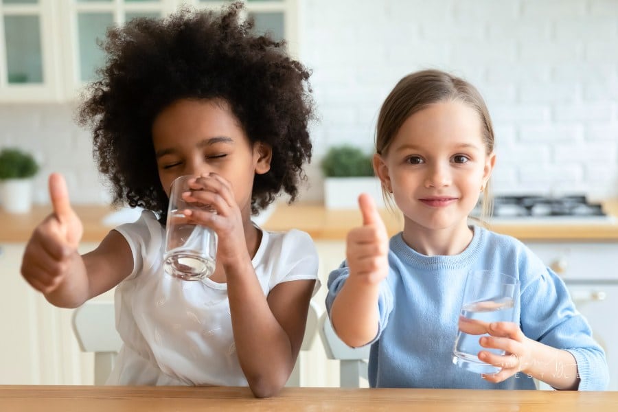 Portrait of happy children enjoying drinking water giving thumbs up