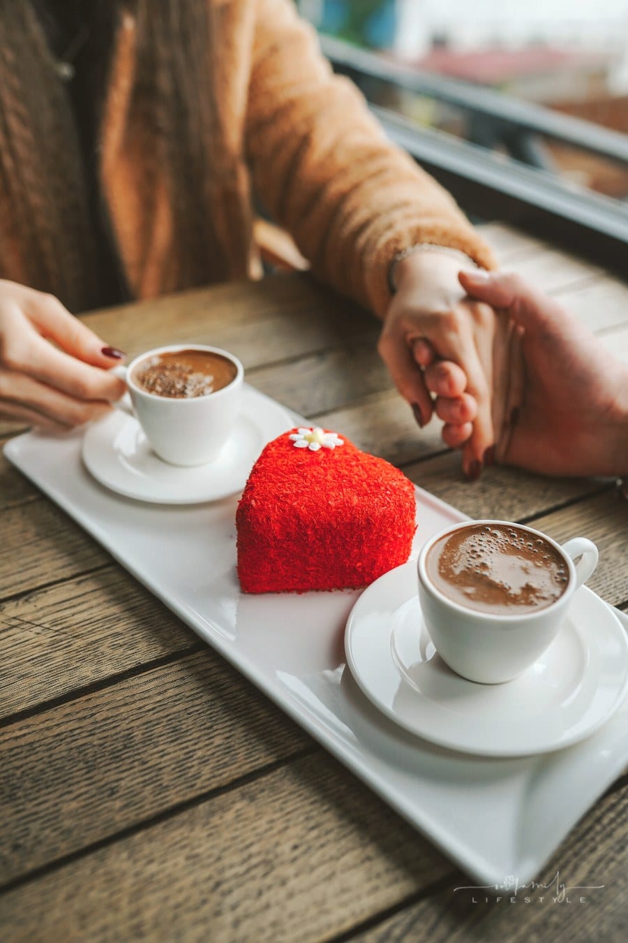 couple holding hands over coffee and red heart-shaped cake