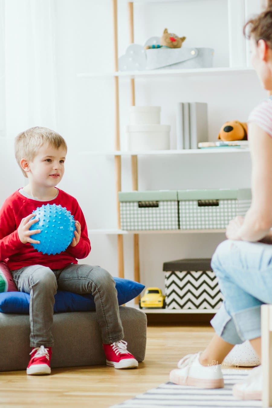 Cute little boy sitting on pouf and holding blue ball during ADHD therapy