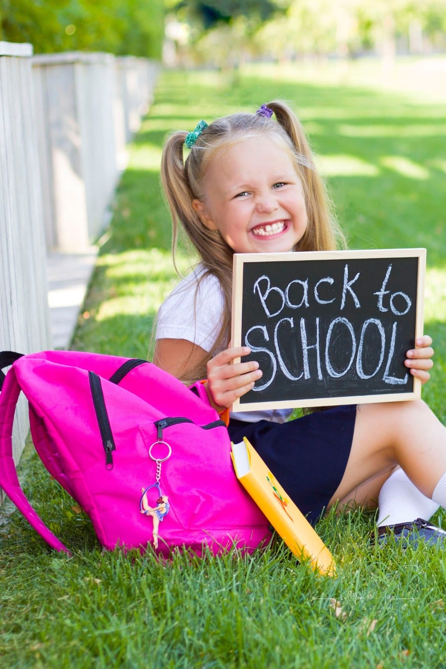 girl sitting on lawn with back to school chalkboard and pink backpack