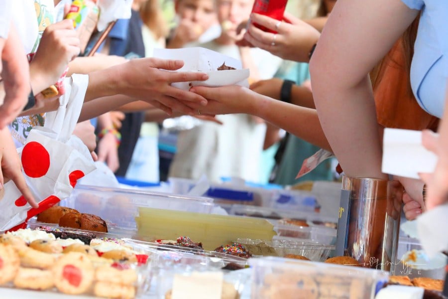A close up of hands and food exchanging at a communty fair, fete or market stall. A typical bake or cake sale.