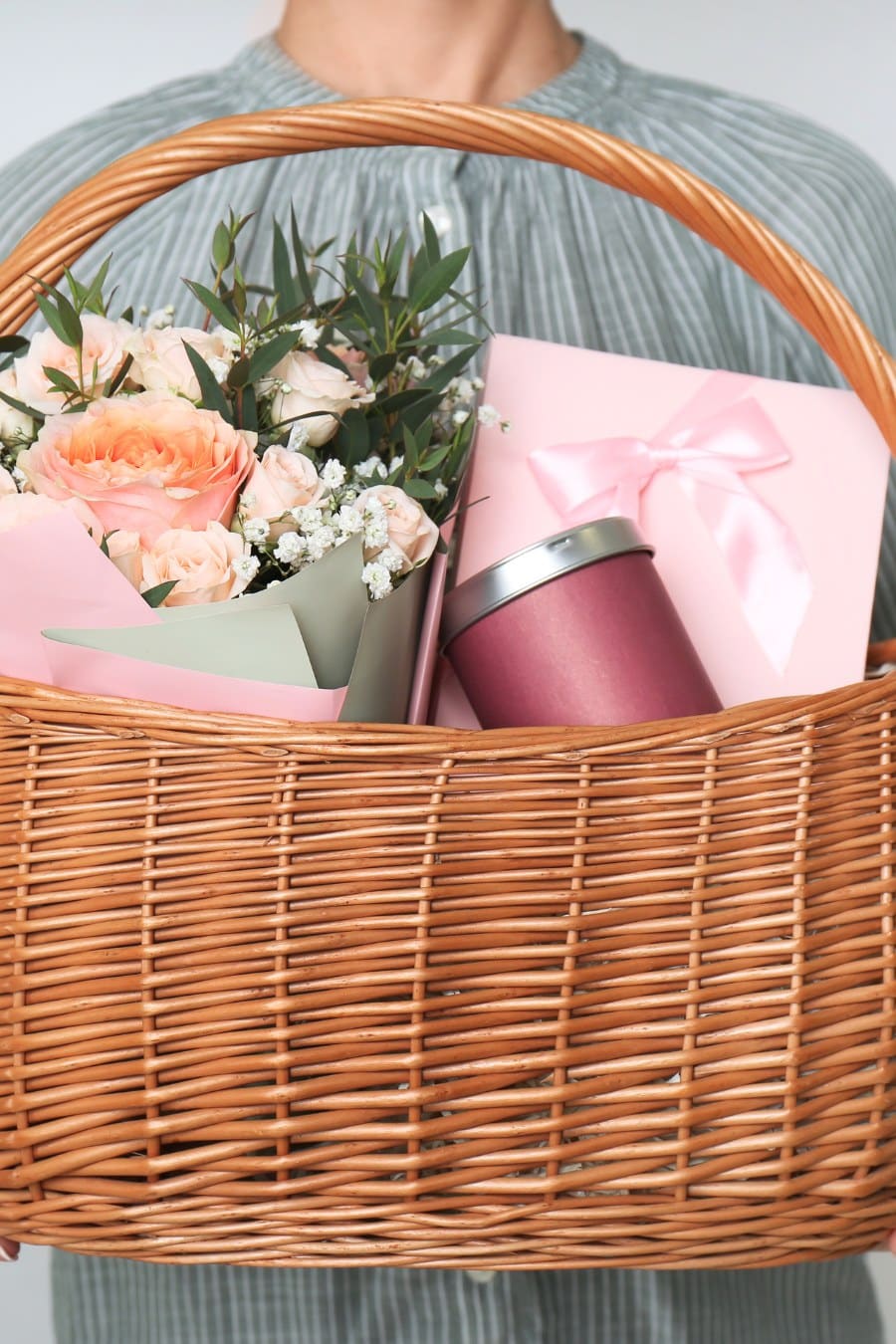Woman Holding Wicker Basket with Different Gifts on Grey Background, Closeup
