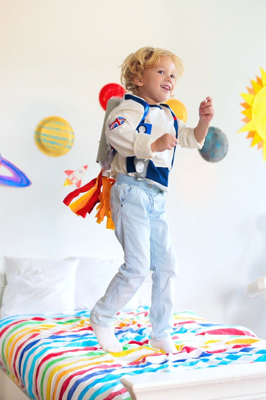 little boy in astronaut space costume jumping on bed with solar system on the wall