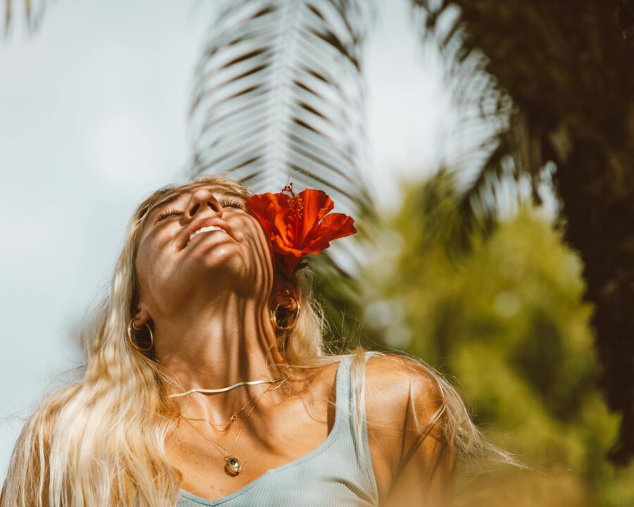 Woman embracing nature's warmth with a red flower accent, surrounded by tropical greenery.