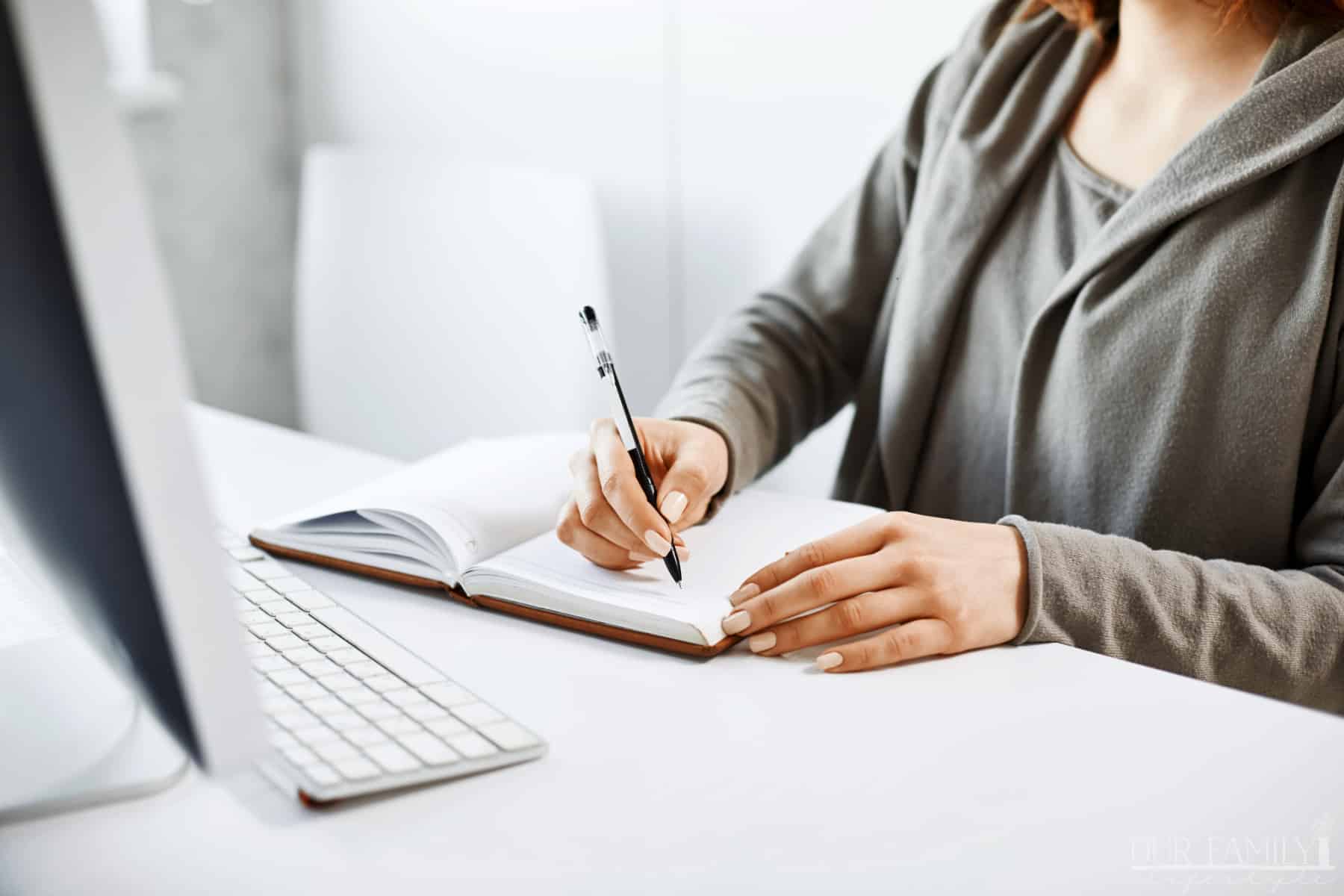 woman-making-notes-in-notebook-looking-at-computer