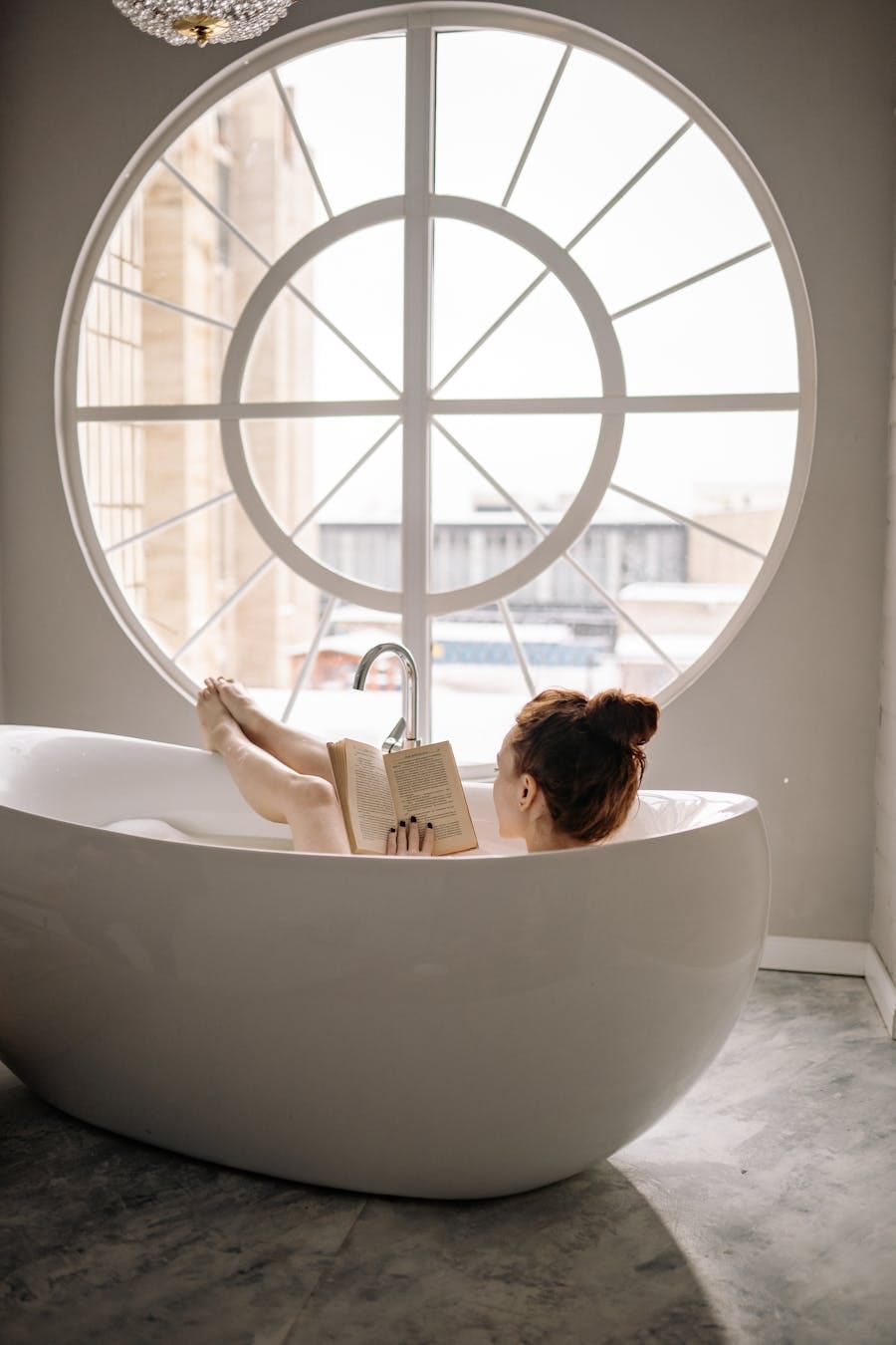 Woman relaxing in a modern bathtub by a large window, enjoying a good book.