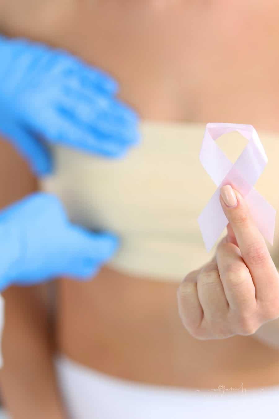 woman holding pink breast cancer awareness ribbon with bandage around her chest