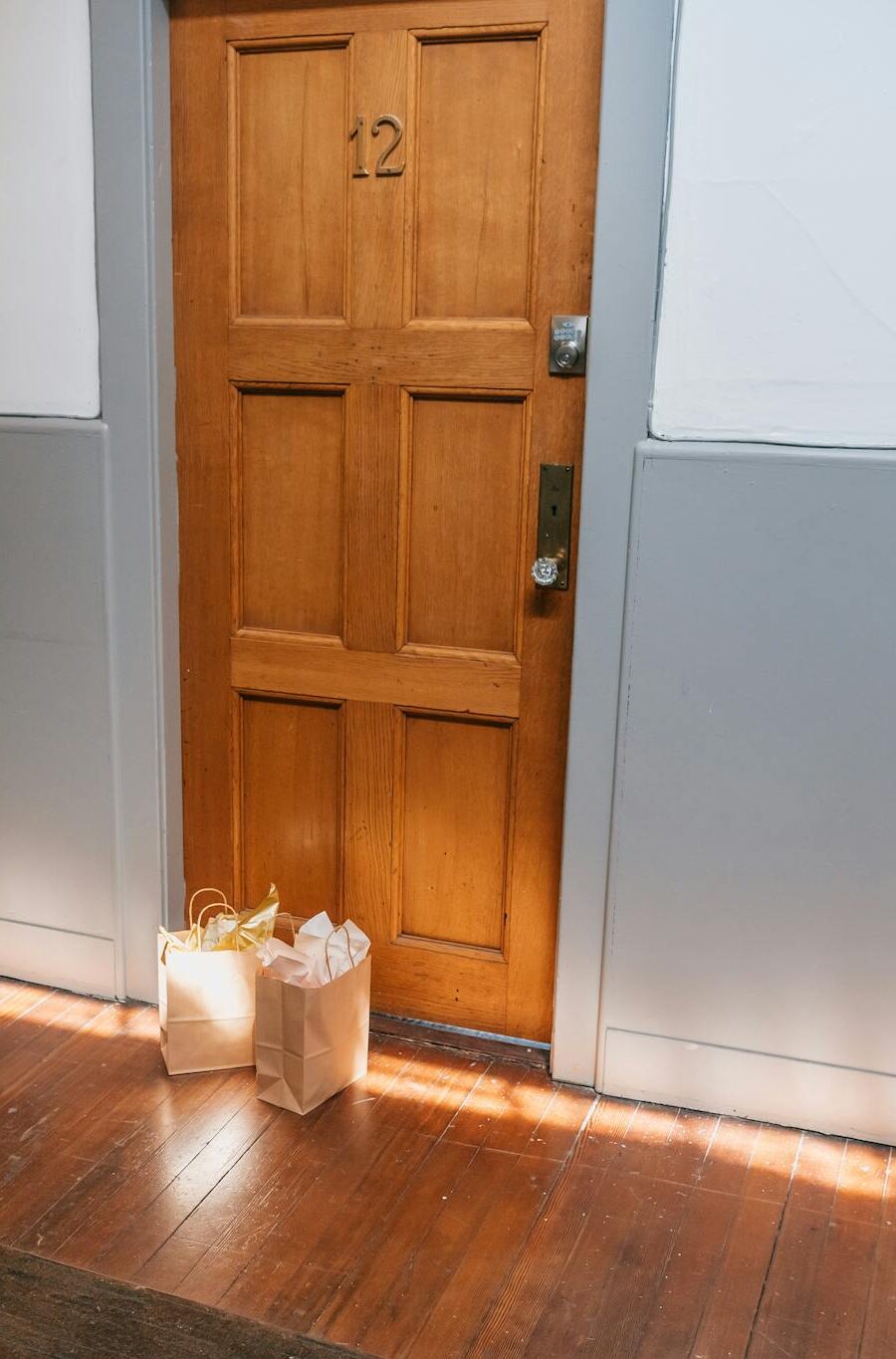 Wooden apartment door with paper shopping bags left outside, basking in warm sunlight.